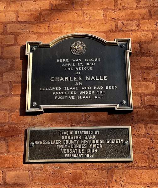 plaque, on red brick building, with shadow from tree