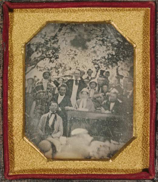 outdoor photograph, abolitionists standing around table, Frederick Douglass seated next to it