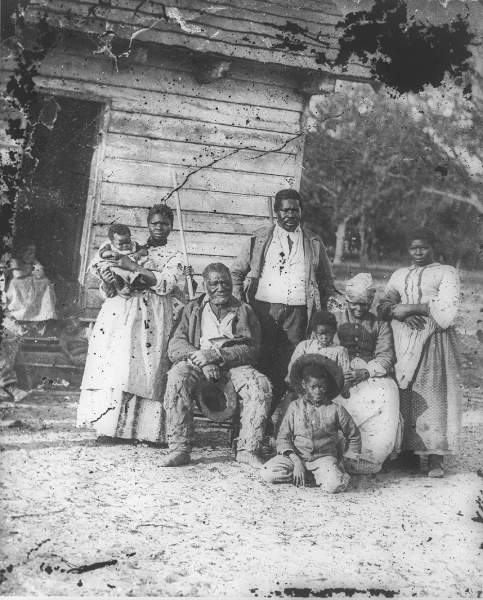 family, men, women, children posing outside cabin