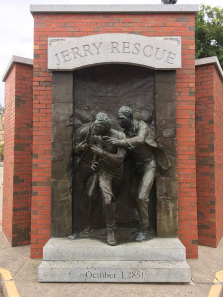 two men, bronze figures, against red brick wall, words Jerry Rescue